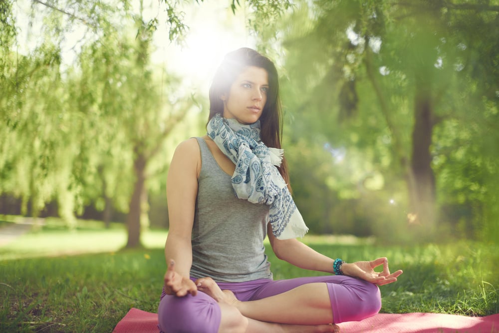 Serene and peaceful woman practicing mindful awareness by meditating in nature with sun flare. Serene and peaceful woman practicing mindful awareness by meditating in nature with sun flare.